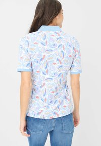 Camicia a maniche corte in tessuto leggero, caratterizzata da un motivo di foglie pastello su fondo azzurro chiaro con colletto e polsini blu uni.