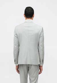 Blazer cinza claro com um padrão de xadrez subtil, ombros estruturados e ventoinha simples. Detalhes adicionais incluem punhos abotoados.