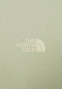 Světle zelené tričko vyrobené z měkké látky, s krémovým potiskem loga "THE NORTH FACE" na levé přední straně.