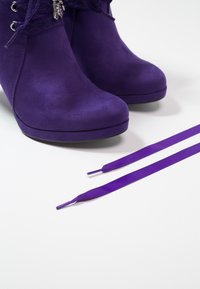 Botines de ante púrpura con puntera redondeada y diseño de cordones, acompañados de cordones púrpuras a juego sobre un fondo blanco.