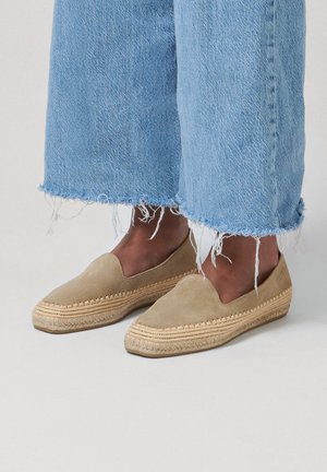 Voeten met tankleurige suède espadrille instap schoenen met geweven jutezolen, gecombineerd met lichtblauwe cropped jeans met rafelige zoom.