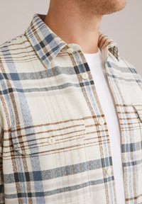 Rutigt flanellskjorta i blå, brun och krämfärgad, med standardkrage och knappstängning, texturerad tyg och en bröstficka.