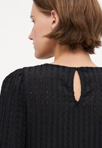 Black textured blouse featuring vertical stripes, scoop neckline with a keyhole opening at the back, and gathered sleeves.