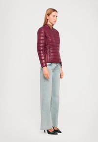 Bordo puffer jakna s patentnim zatvaračem, s quilted dizajnom i bočnim džepovima, u kombinaciji s svijetloplavim širokim trapericama i crnim potpeticama.