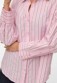 Camicia a righe rosa con bottoni, realizzata in un tessuto leggero, caratterizzata da righe verticali bianche e marroni, con maniche lunghe e polsini con bottoni.