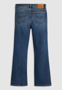 Jean flare en denim bleu foncé avec une finition texturée subtile, dotée de deux poches arrière et d'un patch logo en cuir marron à la taille.