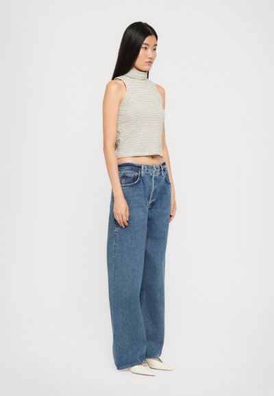 Striped sleeveless crop top with a high neckline, paired with wide-leg blue denim jeans and white pointed-toe shoes.