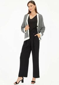 Czarny i biały kardigan w paski z kontrastowym wykończeniem, w połączeniu z wysokimi czarnymi spodniami i czarnymi sandałami na obcasie. Gładkie faktury w całej stylizacji.