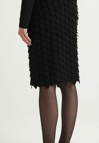 Jupe noire ajustée présentant un motif texturé de formes écailleuses superposées, confectionnée dans un matériau extensible, avec une finition lisse.