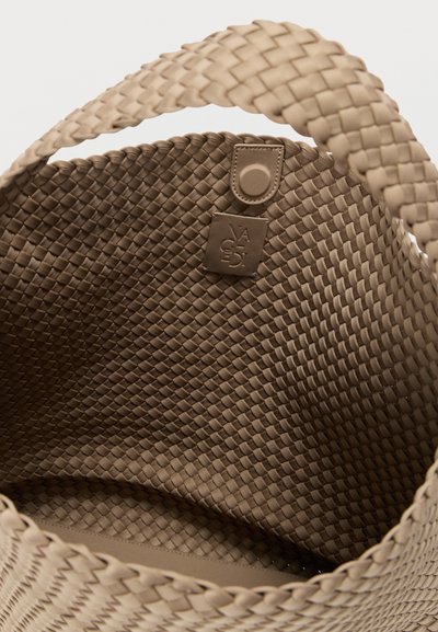 Πλεκτή τσάντα ώμου σε καφέ απόχρωση με λείο εσωτερικό, διακοσμητική ετικέτα και γερά, επίπεδα χερούλια. Υφή σε όλο το σχέδιο.