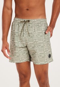 Zwemshorts van een groene stof met patroon, voorzien van een tailleband met trekkoord, zijzakken en een zwart logo-embleem.