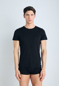 Camiseta de algodón negra de mangas cortas, con cuello redondo y una textura suave; combinada con bóxer negros ajustados. Diseño simple, con mínima marca.