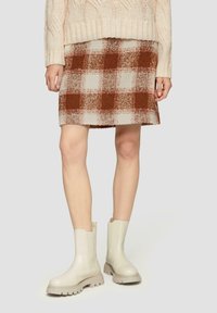Gewebter kariierter Rock in Braun und Creme mit einer strukturierten Oberfläche, kombiniert mit cremefarbenen Ankle Boots mit stabilen Sohlen und einer glatten Oberfläche.