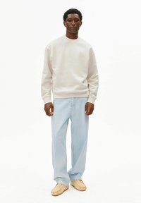 Felpa grigio chiaro con scollo a girocollo, abbinata a jeans larghi a zampa sbiaditi blu e mocassini chiari. Texture liscia.