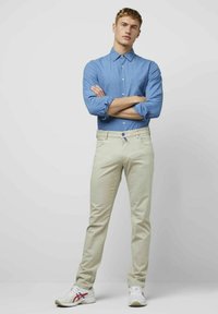 Lichtblauwe blouse met kraag, gecombineerd met crèmekleurige broeken en witte sneakers met rode en blauwe accenten.