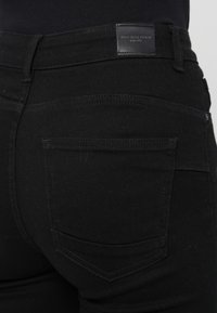 Mustad denim püksid siledat tekstuuri, millel on kaks tagakotti ja nahklabel vöökoht. Tootel on minimaalsed õmblusdetailid.