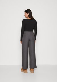 Zwart top met lange mouwen gecombineerd met grijze wijde broek. De broek heeft een hoge tailleband, een soepele textuur en is enkel-lang.