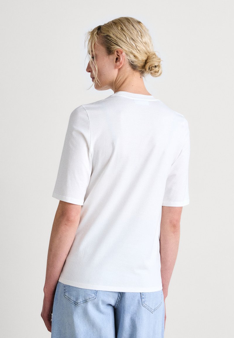 Biała bawełniana koszulka z krótkim rękawem, okrągłym dekoltem i subtelną fakturą. Posiada luźny krój i płaskie szwy.