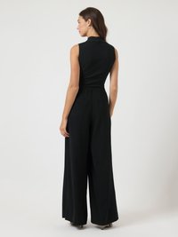 Μαύρο αμάνικο ολόσωμο φόρεμα με εφαρμοστό κορσάζ και παντελόνι σε φαρδιά γραμμή. Κατασκευασμένο από μαλακό ύφασμα, διαθέτει υψηλό γιακά και δύο πλάγιες τσέπες.