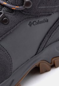 Μποτάκι πεζοπορίας σε μαύρο και γκρι με καουτσ ούκ σόλα, υφή σουέτ, κορδόνι με πορτοκαλί λεπτομέρειες και λογότυπο της μάρκας Columbia στο πλάι.