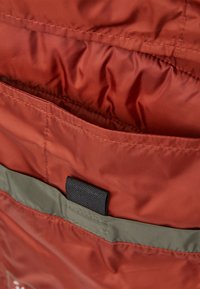 Czerwony materiał o gładkiej fakturze ma zielony pas na dole i małą czarną łatę, zaprojektowaną jako otwarcie kieszeni na krawędzi.