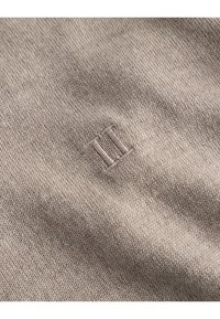 Tessuto a maglia beige con una texture liscia. Presenta un piccolo ricamo "III" in una tonalità di beige leggermente più scura. Design semplice e minimalista.