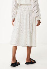 Vit bomullsklänning med hålmönster, knälång, elastisk midja, långa ärmar, kombinerad med svarta platta sandaler. Texturerad och lätt.