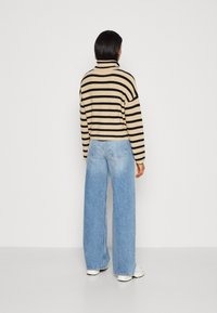 Pull à col roulé beige et noir à rayures avec des manches larges, associé à un jean bleu clair taille haute à jambes larges et des baskets blanches.