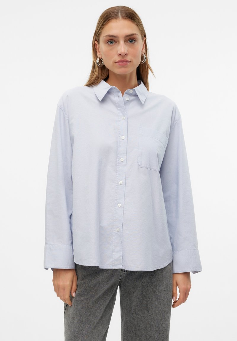 Camicia azzurra chiara con bottone in cotone, dotata di colletto, maniche lunghe, tasca sul petto singola e orlo dritto. Nota per la sua morbidezza.