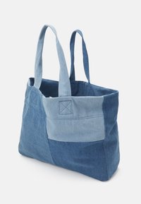 Denim tote taske med et patchworkdesign i forskellige nuancer af blå, med to kraftige håndtag og syede detaljer på siderne.