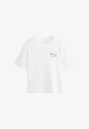 T-shirt blanc à manches courtes avec col rond et petit texte noir en haut à gauche indiquant, "NE ME SUIVEZ PAS, JE SUIS PERDU AUSSI."