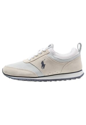 Zapatilla baja beige y blanca con paneles de malla y ante, cordones blancos, suela negra y un logo de jugador de polo negro en el lateral.