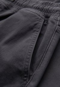 Gros plan sur un tissu gris foncé montrant une poche avec des coutures détaillées et une ceinture élastique sur un vêtement.