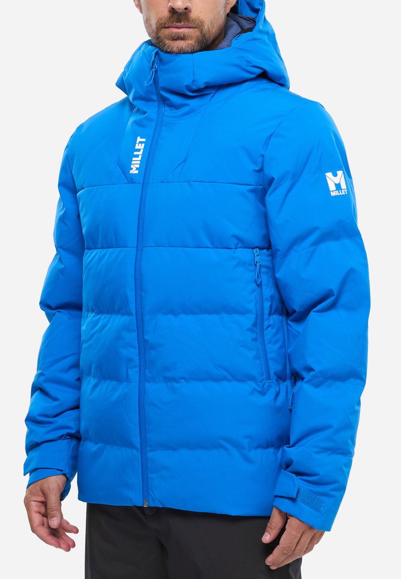 Blaues Puffer-Jackett mit gesteppter Optik, Reißverschluss vorne, verstellbare Kapuze und Logo auf der linken Schulter. Glattes, isoliertes Material.