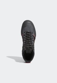 Zapatillas de ante negro con material texturizado, cordones negros resistentes, acentos rojos y suela de goma estriada, con una lengüeta en el talón.