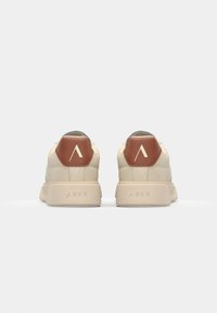 Sneakers beige con finitura testurizzata, dotate di un dettaglio a forma di esagono marrone sul tacco e suola bianca. Marchio "ARKK" sulla suola.