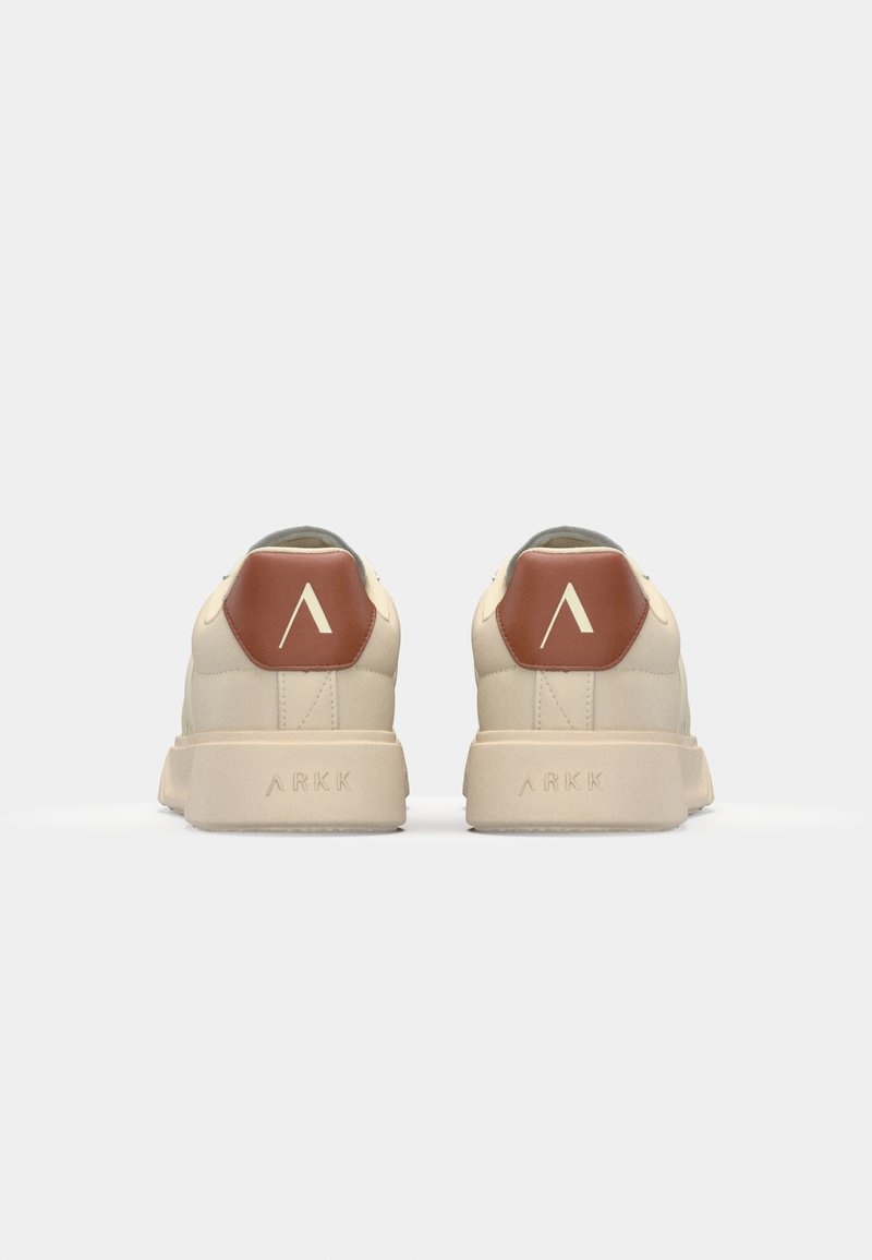 Zapatillas beige con un acabado texturizado, que cuentan con un detalle en el talón hexagonal marrón y una suela blanca. Marca "ARKK" en la suela.