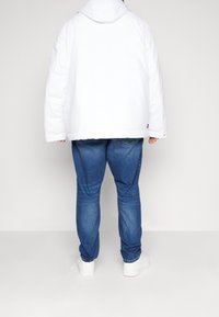 Hvid puffjakke med hætte, kombineret med blå denimjeans og hvide sneakers. Jakken har en loose fit og en quiltet tekstur.