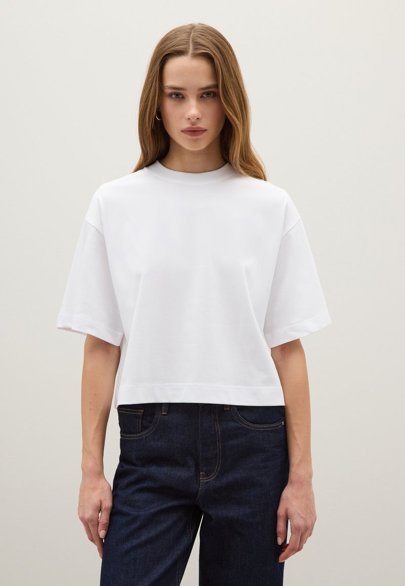Witte cropped t-shirt met korte mouwen, ronde halslijn en een gladde textuur. Gecombineerd met donkerblauwe denim jeans.