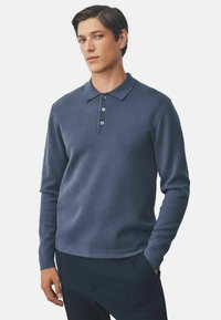 Navy long-sleeve polo shirt made of textured fabric, featuring a three-button placket and a classic collar. Styled with a relaxed fit.