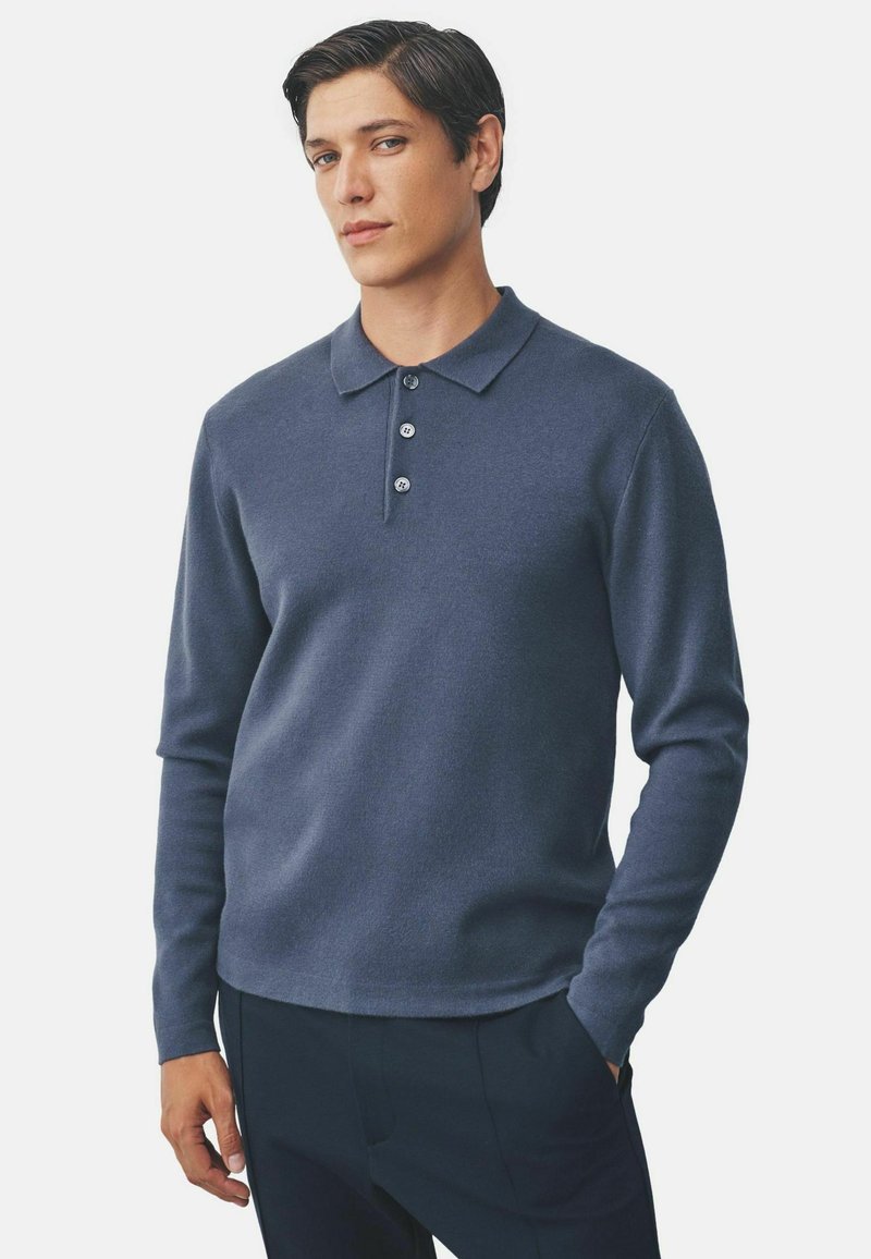 Navy long-sleeve polo shirt made of textured fabric, featuring a three-button placket and a classic collar. Styled with a relaxed fit.