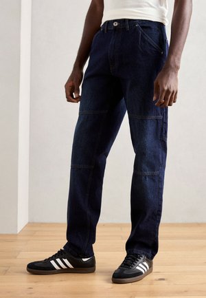 Dark blue denim cargo pants with a straight fit, featuring patch pockets, visible stitching, and a button closure. Paired with black sneakers.
