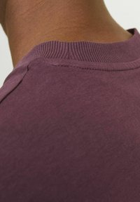 Camiseta de cuello redondo morada con un escote acanalado y material suave, que presenta una textura lisa con costuras mínimas.