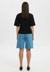 Zwart shirt met korte mouwen en een getailleerd ontwerp, gecombineerd met lichtblauwe denim Bermuda-shorts in een klassieke vijf-pocketstijl.