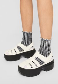 Platform sandals in white with cut-out straps, paired with black and white houndstooth patterned socks. Accented with a textured black sole.