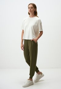 Witte cropped t-shirt en olijfgroene tapered broek met zijzakken, gecombineerd met witte sneakers. Eenvoudige, relaxte pasvorm en zachte textuur.