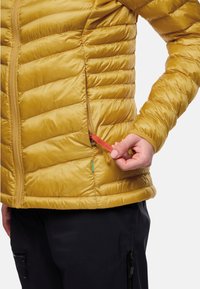 Gelpaddedte Jacke mit gestepptem Design. Verfügt über seitliche Reißverschlusstaschen und einen sichtbaren Zugriegel, abgebildet über schwarzen Hosen getragen.