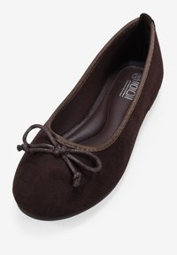 Bailarina de ante marrón con punta redonda, que presenta un lazo decorativo de cordón marrón en la parte delantera y un forro interior suave.