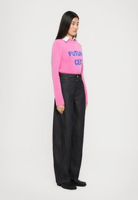 Rosa strikkegenser med blå tekst "FUTURE CEO", kombinert med høyt liv mørk denim vide bukser og svarte ankelstøvler.