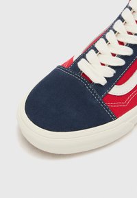 Sneaker with a navy suede toe cap, red canvas sides, and white laces. Features a white logo stripe and cream-colored rubber sole.